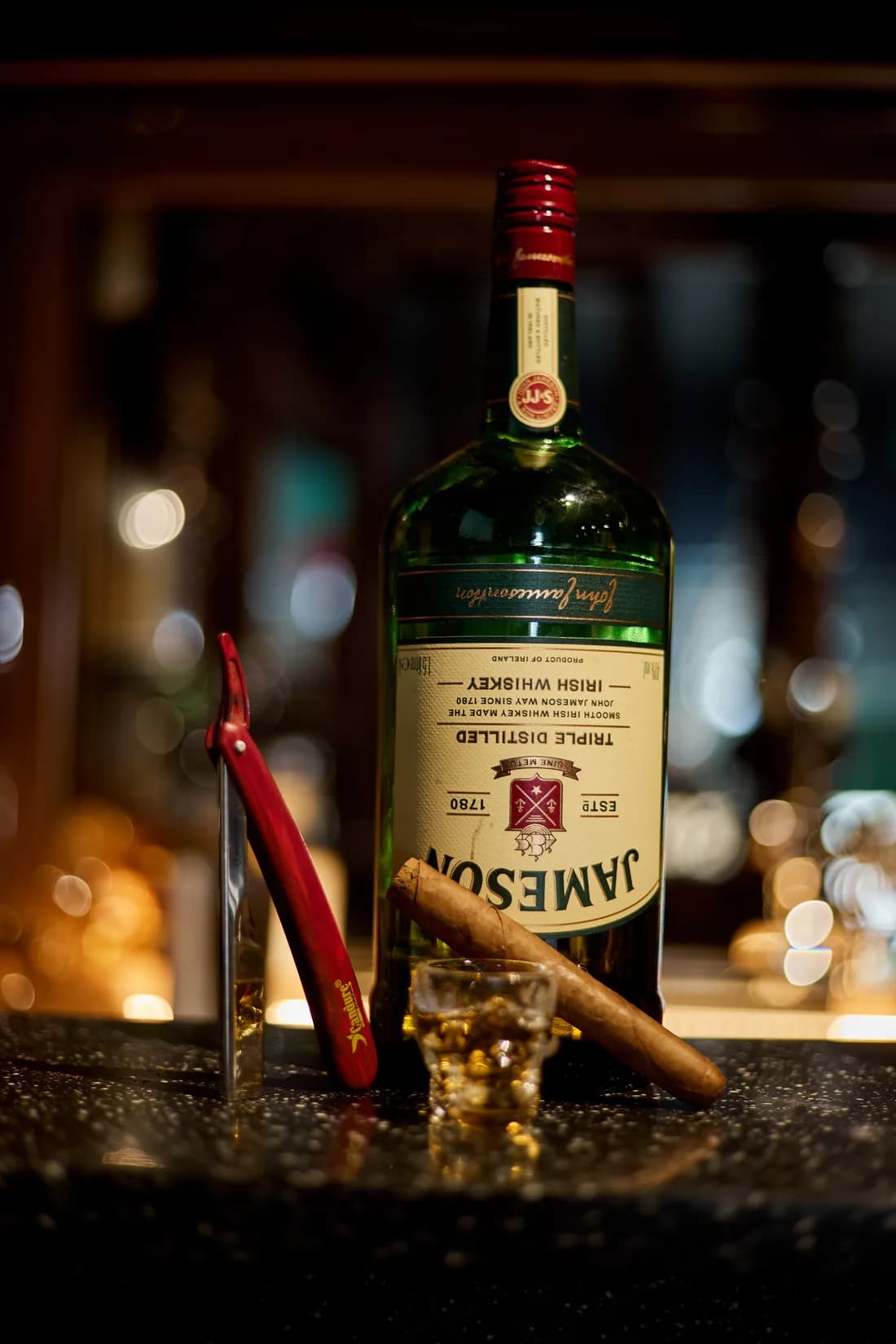 An open cut-throat razor on the bar beside a bottle and a cigar